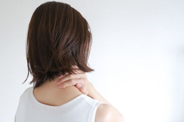 肩こりに悩む女性が首に手を当てている後ろ姿